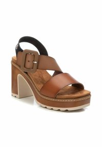 Sandalias de tacón de cuero marrón con un diseño de tiras cruzadas, una hebilla cuadrada ancha y una suela de plataforma resistente con un acabado texturizado.