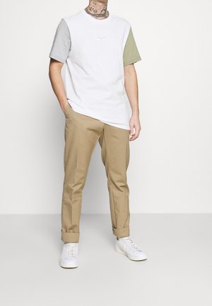 Biała i szara koszulka z zielonym rękawem, z małym logo; w komplecie z beżowymi spodniami i białymi trampkami. Prosty, casualowy design.