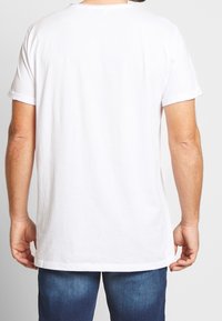 Hvid bomulds t-shirt med korte, rullede ærmer og lige pasform. Bagsiden har en ensfarvet tekstur uden grafik eller mønstre.