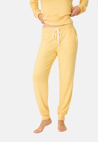 Pantaloni della tuta gialli in cotone con vita elastica, cordoncino e caviglie a costine; presenta una piccola ricamatura floreale sul lato.
