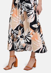 Mekko, jossa on musta, valkoinen ja persikkainen trooppinen lehtikuvio, yhdistettynä oransseihin paksupohjaisiin sandaaleihin, joissa on ohuet nilkkavyöt.