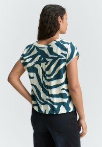 T-shirt à manches courtes avec un motif zèbre teal et crème, à coupe décontractée et avec un pli dans le dos.