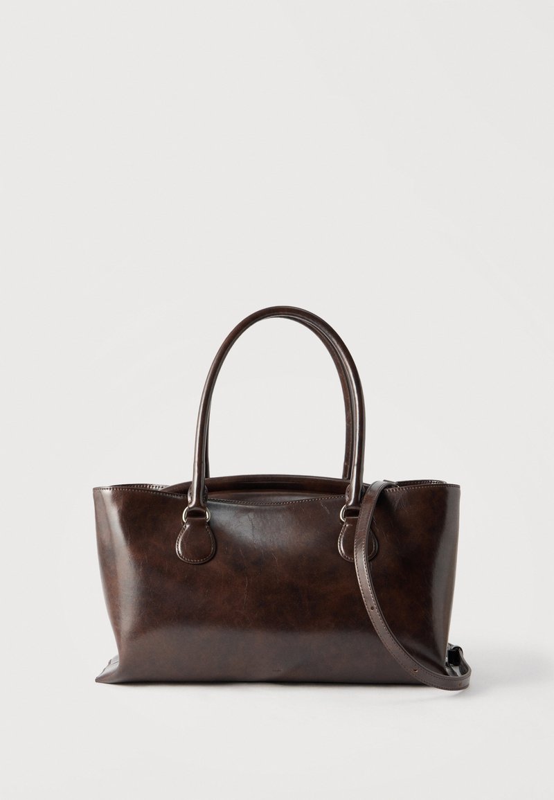 Σκούρα καφέ δερμάτινη τσάντα με διπλούς στρογγυλούς χειρολαβές και αφαιρούμενο ιμάντα ώμου, τοποθετημένη σε απλό λευκό φόντο.