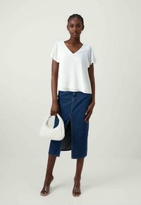 Hvid V-hals top med korte flæseærmer, parret med en denim midi-skjørt med en frontslids. Hvid quiltet håndtaske og brune sandaler.
