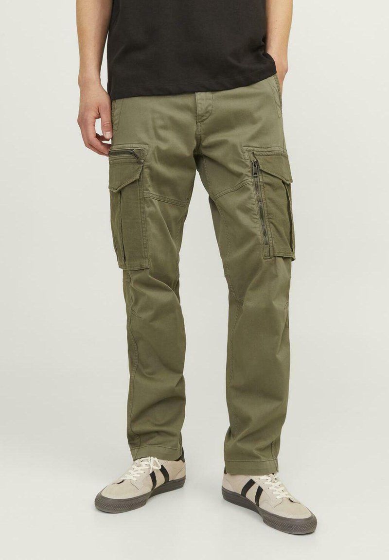 Olive green cargo pants with multiple side pockets, zip closures, and a fitted design. Worn with light-colored shoes featuring black stripes.