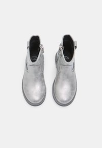 Botines metálicos plateados hasta el tobillo con una textura suave, que cuentan con un cierre lateral y punta redonda. Las suelas son oscuras y tienen un dibujo mínimo.