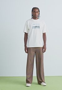 White cotton t-shirt with a graphic design on the front, paired with plaid loose-fitting trousers in shades of brown and cream.