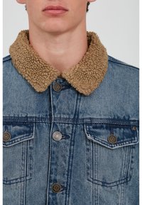 Denim jacket featuring a tan faux shearling collar, button front, and two chest pockets with metal accents. Wash indicates a faded look.