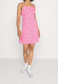 Pink sundress with yellow and blue floral pattern, spaghetti straps, fitted bodice, flowing skirt. Worn with white socks and silver-green sneakers.