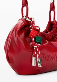 Geantă de mână din piele roșie cu formă moale și rotunjită. Are accente împletite cu blocuri roșii și verzi, accesorii din argint și detalii strânse.