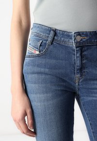 Blekta blå denimjeans med en figurnära passform, synlig sömnad, metallknappstängning och en liten etikett på bakfickan.