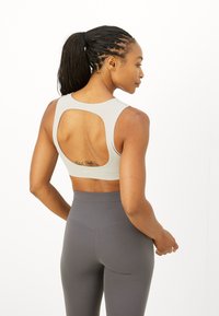 Sujeción deportiva gris claro con un diseño de espalda abierta; combinado con leggings oscuros de tiro alto, textura suave y forma ajustada.