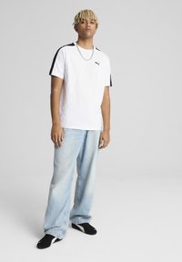 Camiseta blanca de manga corta con acentos laterales negros y el logo de Puma, combinada con jeans de corte holgado azul claros y zapatos negros.
