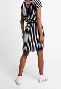 Navy and white striped dress with short sleeves, cinched waist, and cut-out back detail, paired with white sneakers.