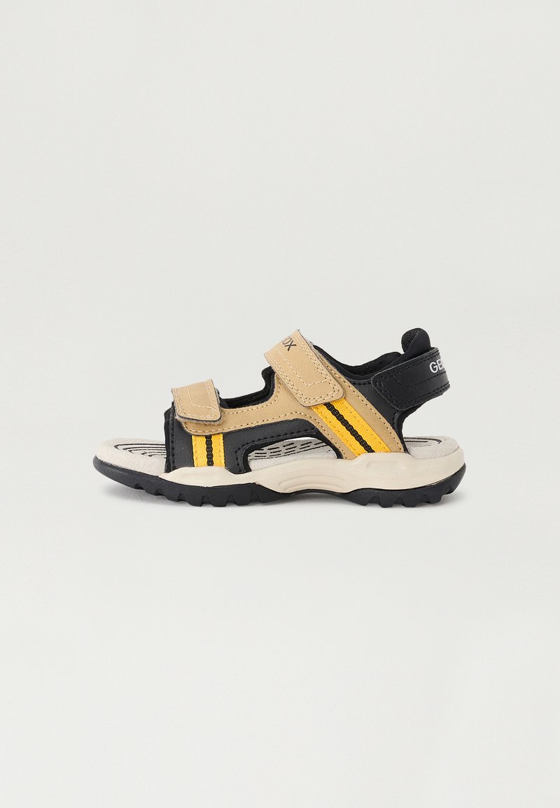 Sporty sandal with a beige and black textile upper, yellow accent stripes, adjustable Velcro straps, and a textured black rubber sole.