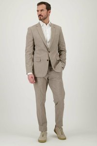 Lichtbruine, geruite pak met een colbert met enkele knopen en bijpassende broek, gecombineerd met een wit shirt en beige sneakers.