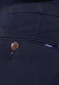 Navyblå bomullsbyxor med en slät yta, en enda brun knapp och en liten vit "Polo"-etikett nära fickans söm.