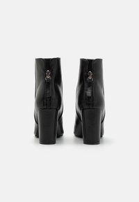 Botine negre din piele cu toc bloc, având un luciu subtil, fermoare la spate și un design elegant. Textură netedă și formă bine definită.