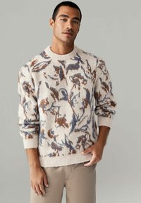 Cream knitted sweater featuring a floral pattern in blue and brown tones, ribbed cuffs, and a round neckline. Soft texture and relaxed fit.