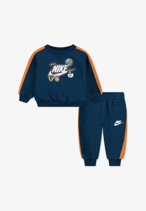 Chándal para niño pequeño en azul marino con rayas laterales naranjas. Presenta un logo y parches en la sudadera. Puños y cinturilla elásticos para mayor comodidad.