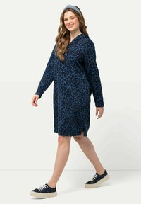 Kapuzenkleid in Marineblau mit blauem Leopardenmuster, mittellang, mit langen Ärmeln, seitlichen Schlitzen, kombiniert mit Marineblauen Sneakers und einem passenden Stirnband.