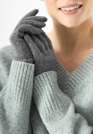 Des gants en laine gris avec des poignets côtelés et une texture douce, associés à un pull gris clair en design col en V.