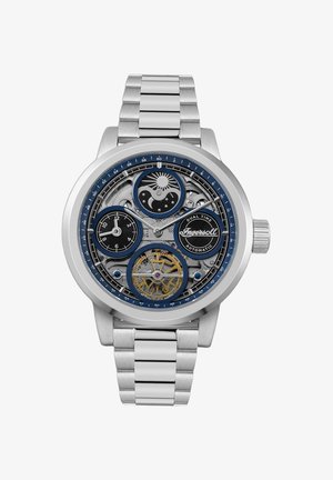 Heren automatisch horloge met een zilveren roestvrijstalen armband, blauwe en zwarte wijzerplaat, zichtbare tandwielen, en dubbele tijdzones aangegeven.