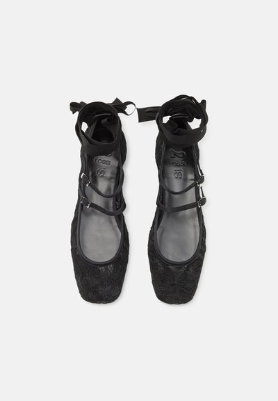 Scarpe flat nere con design testurizzato floreale, punta rotonda e cinturini alla caviglia. Il materiale sembra morbido con una fodera interna liscia.