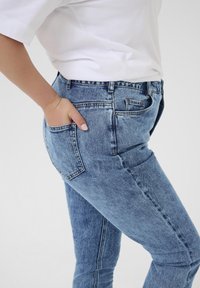 Vaqueros de mezclilla azul con un corte slim, cinco bolsillos y un ligero desgaste. Cuentan con una cintura de altura media y costuras en contraste a lo largo de las costuras.