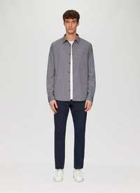 Een button-up shirt in een zwart-wit geometrisch patroon, met lange mouwen, gecombineerd met marineblauwe broek en witte sneakers. Soepele stoftextuur.