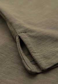 Tessuto in cotone verde oliva con trama a costine, caratterizzato da un orlo arrotolato e una fessura laterale per un movimento migliorato. Design semplice e minimalista.