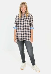Zwart-wit geblokte shirt met opgerolde blauwe mouwen, knoopdetails en een zak, gecombineerd met grijze jeans en witte sneakers.