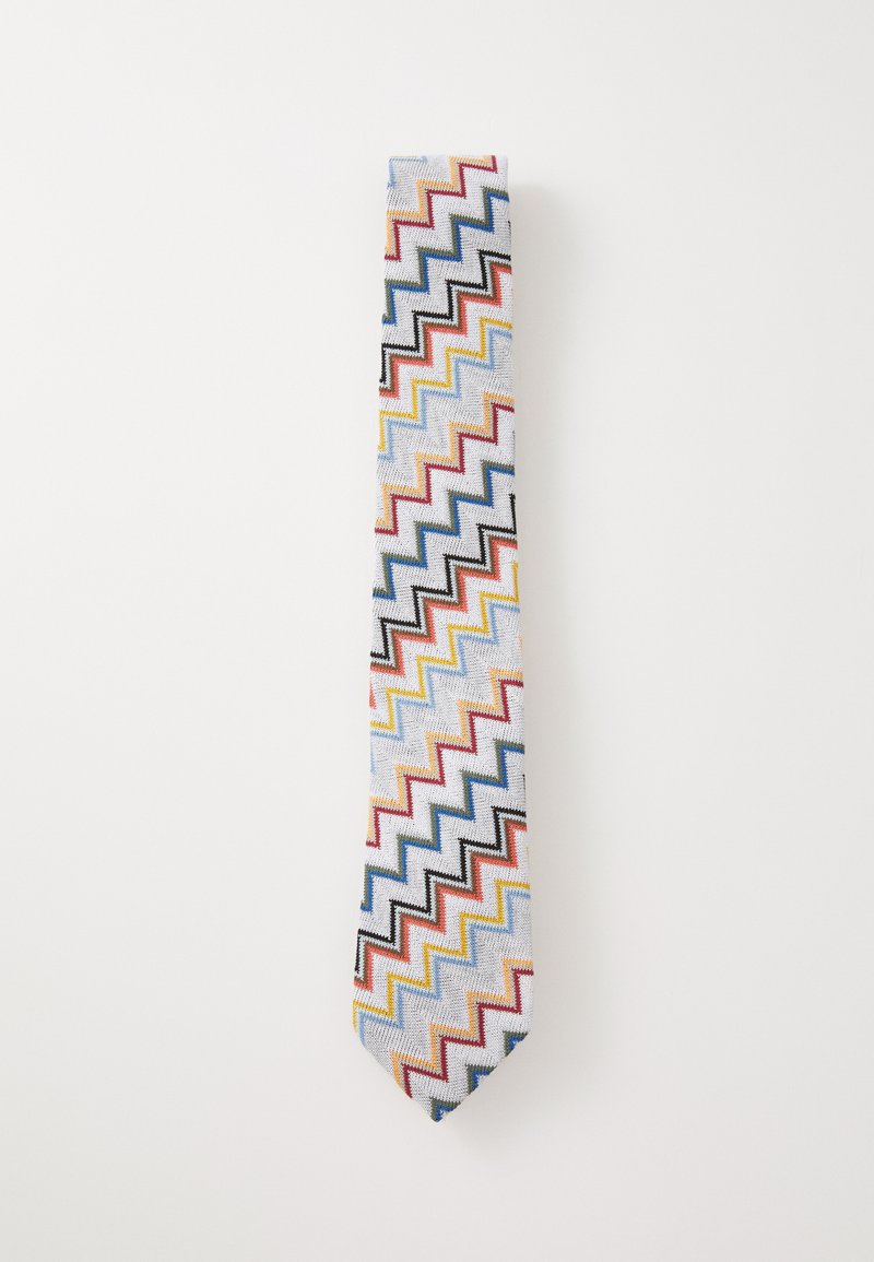 Rakstainā kaklasaita ar zigzaga dizainu sarkanā, zilā, dzeltenā un melnā krāsā uz gaiši zila fona, izgatavota no auduma ar gludu tekstūru.