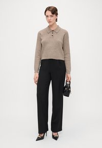 Beige knit polo sweater with three brown buttons, paired with high-waisted black trousers. Black handbag and pointed heels complete the look.