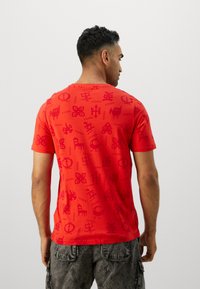 Rød kortærmet t-shirt med et gentagent mønster af symboler og designs, lavet af blødt stof med en afslappet pasform.