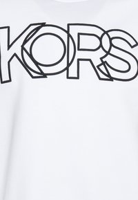 Camiseta blanca con letras negras audaces que deletrean "KORS", con acentos circulares integrados en el diseño. Textura de tela suave.