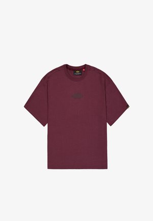 Dunkelrotes kurzärmeliges T-Shirt mit dem "Alpha Industries"-Logo mittig auf der Brust und einem kleinen schwarz-gelben Etikett am linken Ärmel.