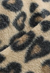 Leopardi-kuosiset kangas, jossa on pehmeä ja pörröinen rakenne. Väriasteikkoon kuuluu beige, musta ja vaaleanruskeat täplät, jotka muodostavat kuvion pinnalle.