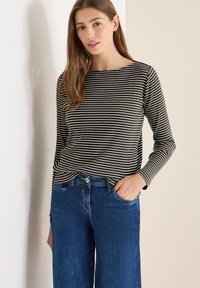 Czarna i biała bluzka w paski z długim rękawem i dekoltem w łódkę, zestawiona z wysokim stanem niebieskich dżinsów, posiadających przednią kieszeń i prosty krój nogawek.