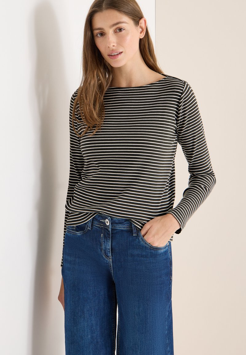 Czarna i biała bluzka w paski z długim rękawem i dekoltem w łódkę, zestawiona z wysokim stanem niebieskich dżinsów, posiadających przednią kieszeń i prosty krój nogawek.