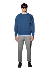 Niebieska bluza z logo "HALO", szare spodnie dresowe, czarne sneakersy i okulary przeciwsłoneczne. Swobodny krój, materiał bawełniany, ściągacze przy mankietach i dolnej krawędzi.