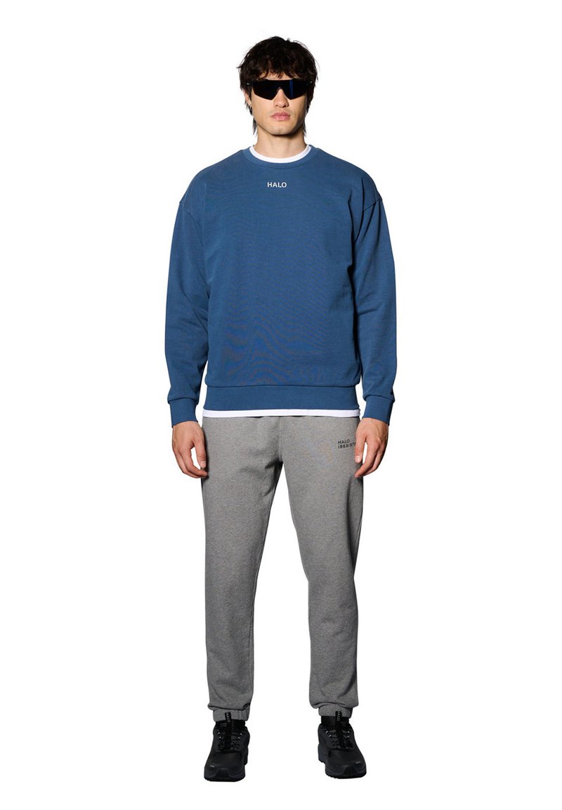 Niebieska bluza z logo "HALO", szare spodnie dresowe, czarne sneakersy i okulary przeciwsłoneczne. Swobodny krój, materiał bawełniany, ściągacze przy mankietach i dolnej krawędzi.