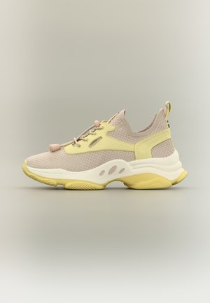 Jasno beżowy i pastelowo żółty sneaker z teksturowaną siateczkową tkaniną, grubą podeszwą, zaciskiem na sznurowadła i pętelką do zakładania na neutralnym tle.