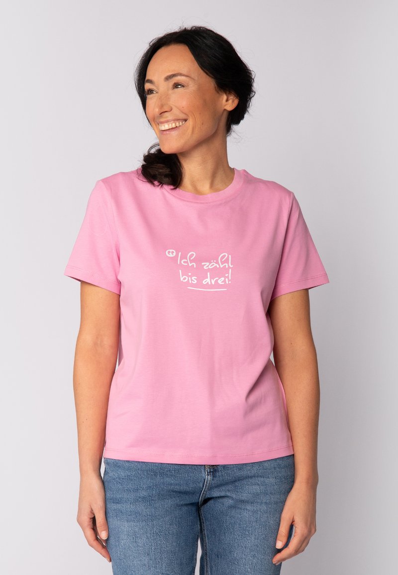 Rosa Baumwoll-T-Shirt mit kurzen Ärmeln, das auf der Vorderseite weißen Text trägt: "Ich zähl bis drei!" Einfaches, lockeres Design.