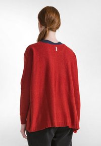Roter Strickpullover mit lockerer Passform. Lange Ärmel und runder Ausschnitt. Hat ein kleines Etikett auf der Rückseite. Weiche Textur und leicht verkürzt.