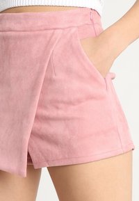 Pantalones cortos de ante rosa con bolsillos laterales, que presentan una textura suave y un diseño plisado. La cinturilla tiene un cierre de cremallera discreto.