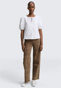 Blusa blanca de mangas abullonadas con un escote de lazo, combinada con pantalones sueltos de estampado de leopardo en tonos marrón claro y zapatillas blancas. Textura suave en toda la prenda.