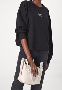 Felpa nera oversize con logo "tommy jeans" sul petto, abbinata a una borsa bianca testurizzata con tracolla recante il logo "Calvin Klein Jeans".