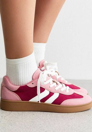 Sneaker in suede rosa e bordeaux con strisce bianche, dotate di una suola in gomma testurizzata e lacci bianchi, abbinate a calze bianche.