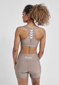 Sostén atlético marrón y pantalones cortos de cintura alta. El sostén tiene acentos en chevron blanco, mientras que los pantalones cortos tienen un logo en la cinturilla.